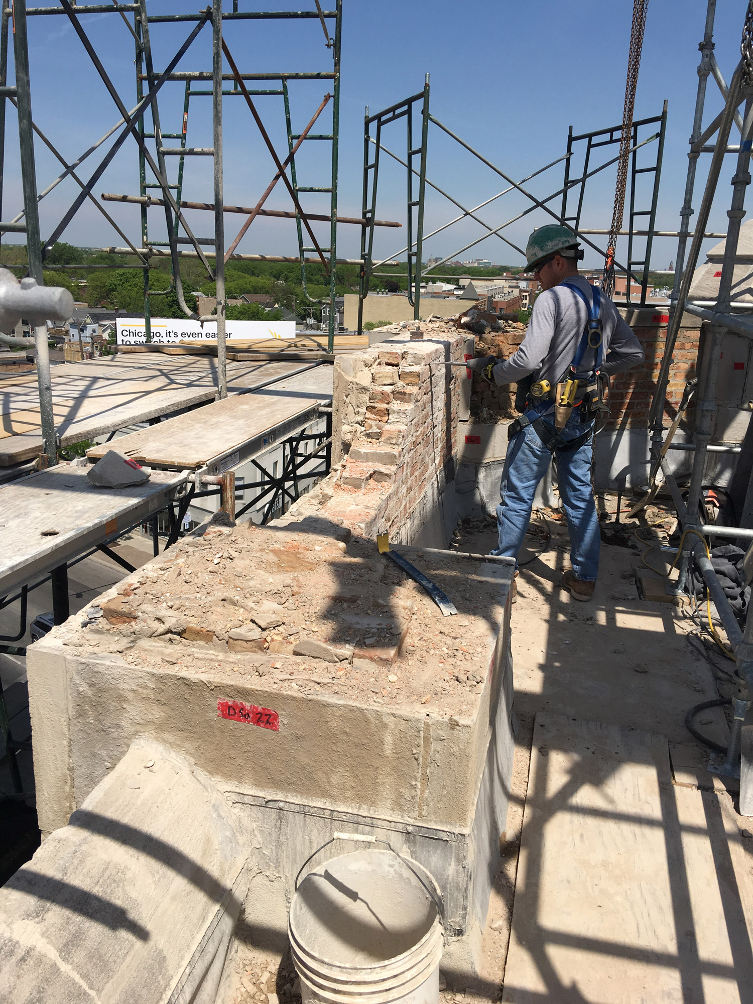 Worker performing brick and masonry wall restoration on scaffolding during construction repair project in Chicago.